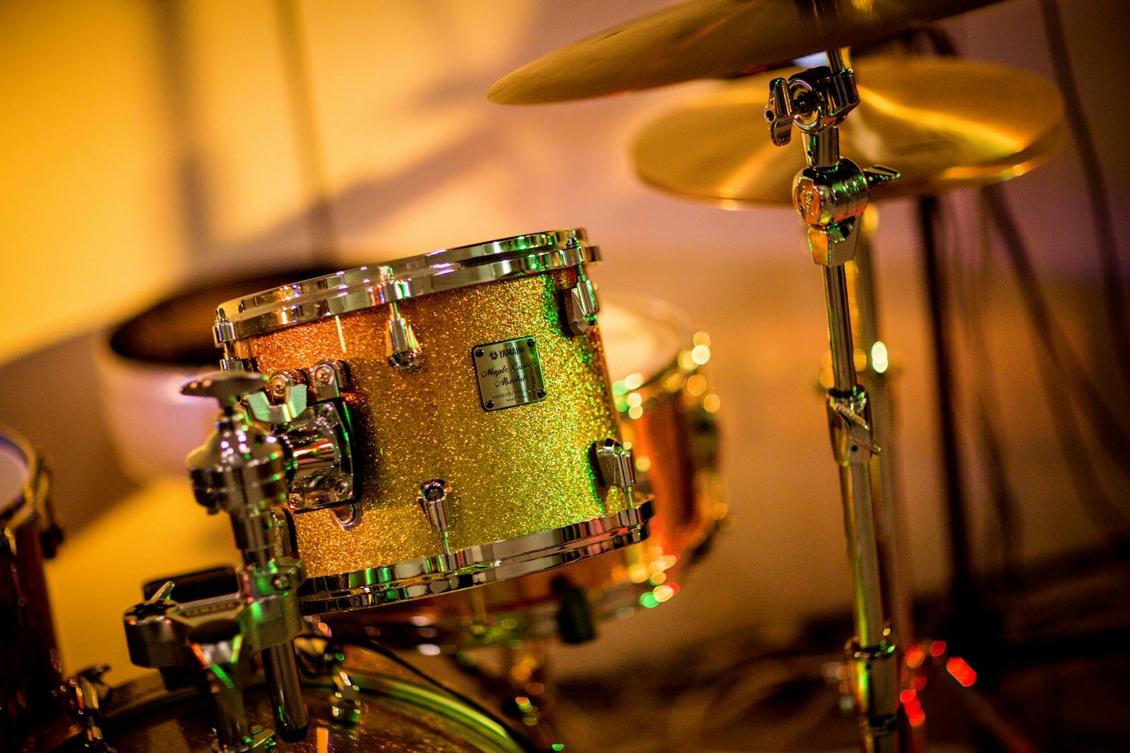 A vibrant close-up photo of a glittery drum set under concert lights, evoking a lively music performance.