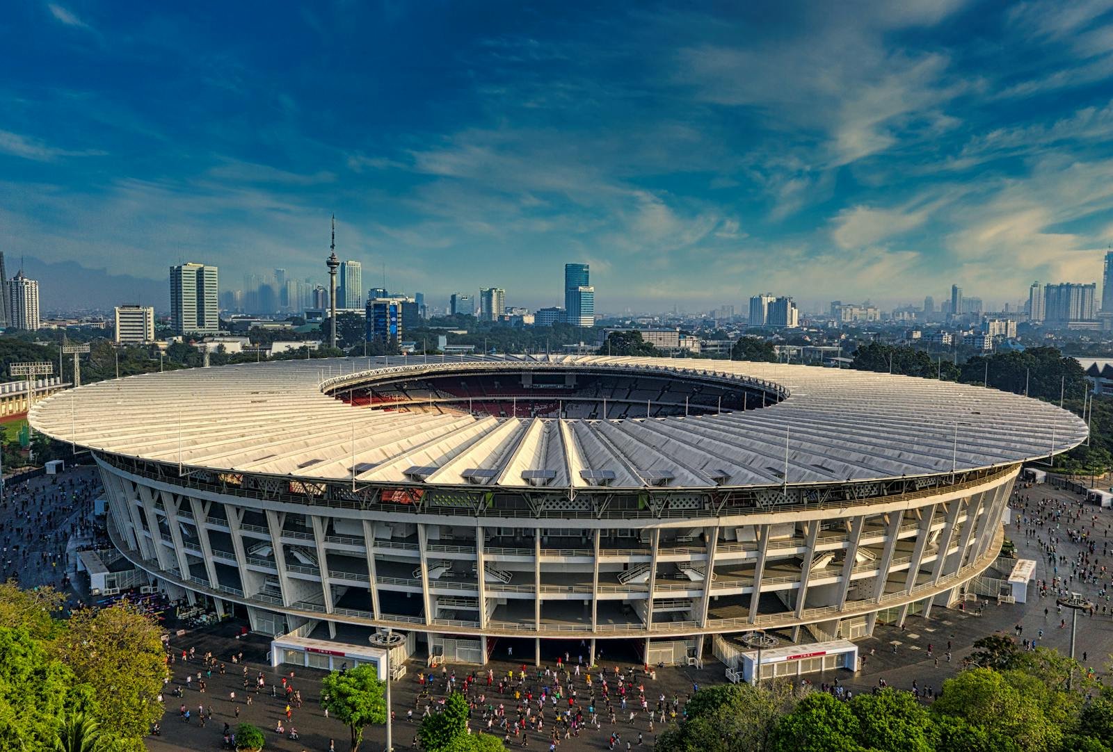 Dramatic aerial view of Gelora Bung Karno Stadium, Jakarta, surrounded by urban skyline.