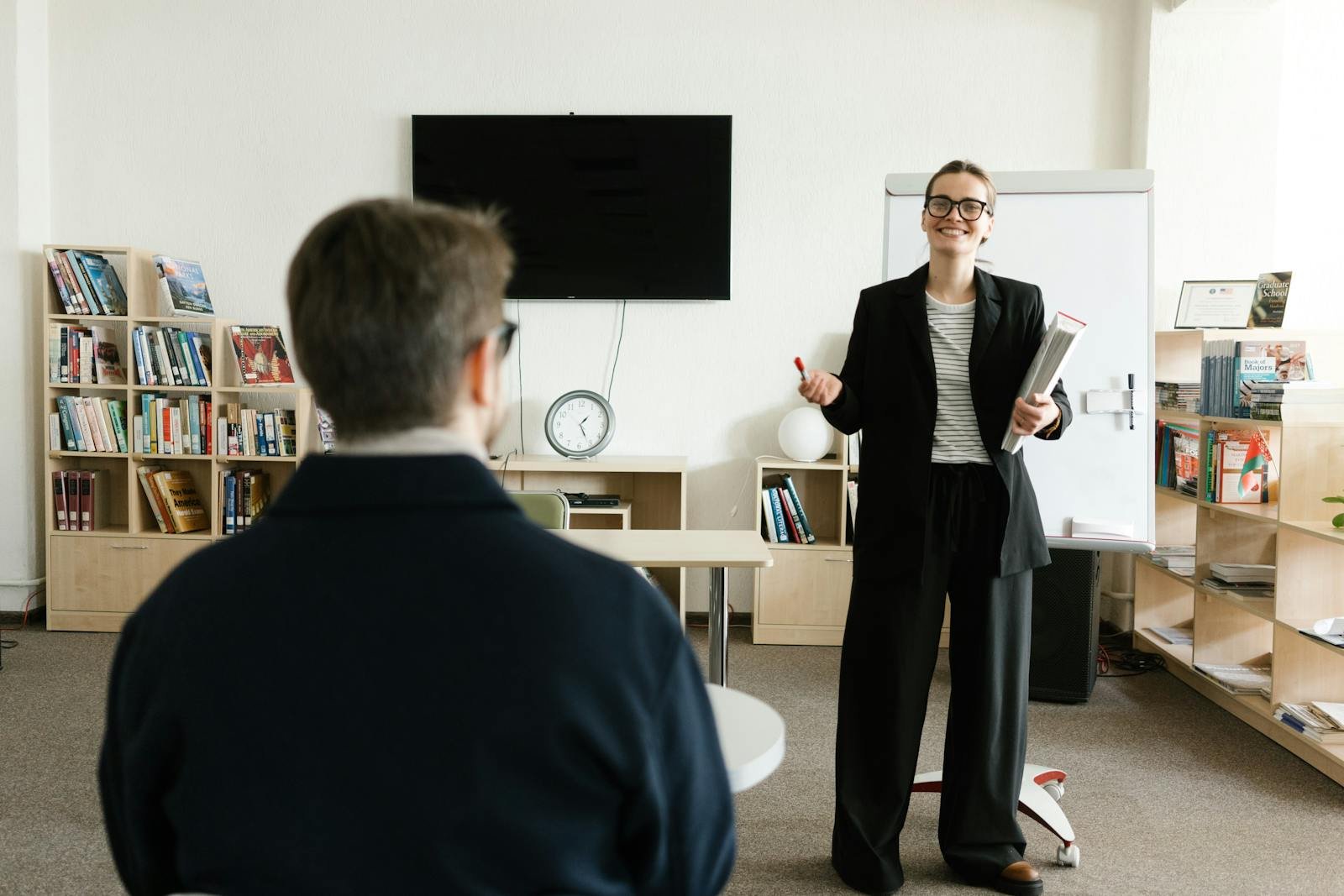 Businesswoman giving presentation in office with bookshelves and clock.