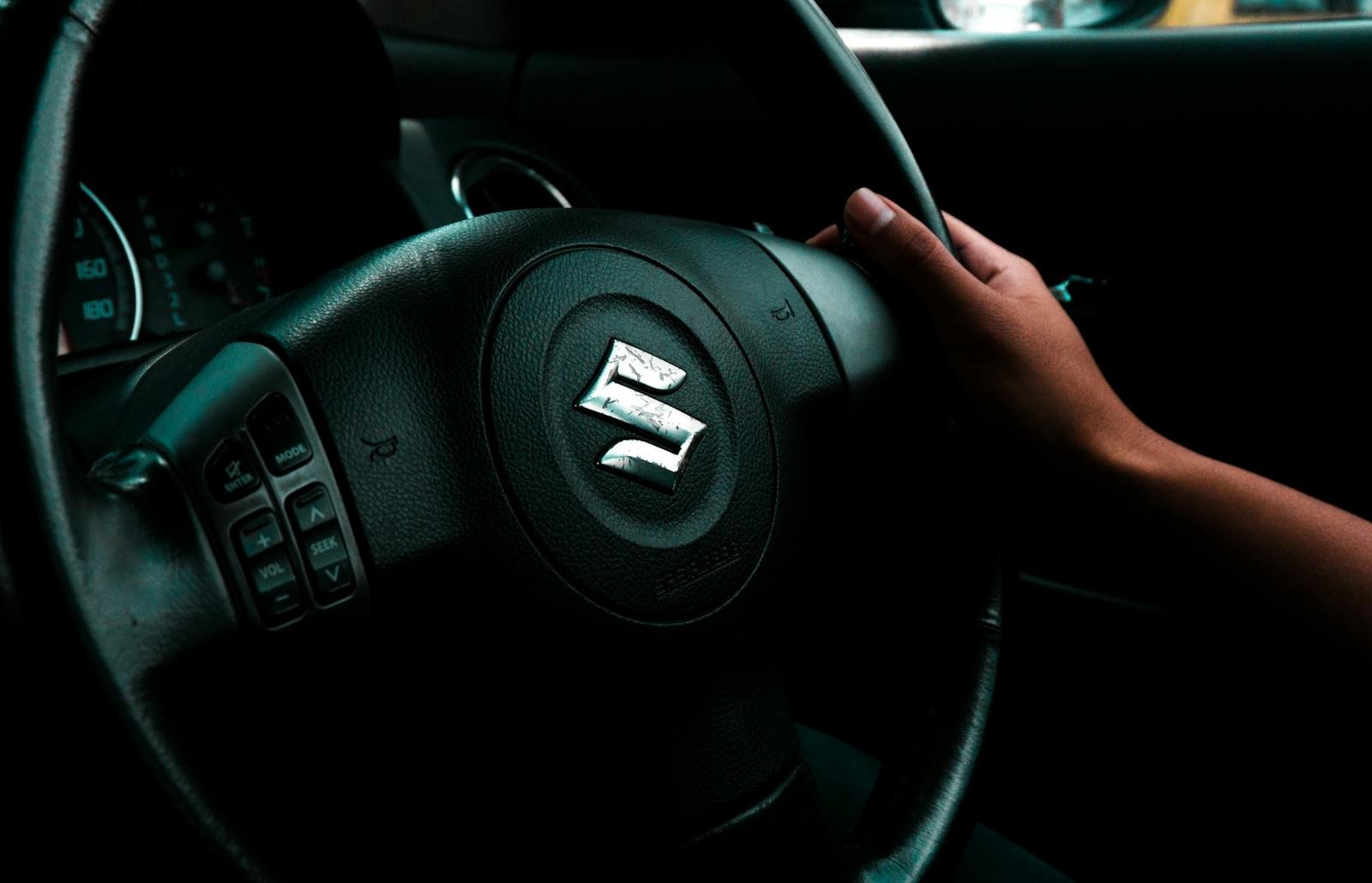 A hand grips the steering wheel of a Suzuki car, highlighting driving control.