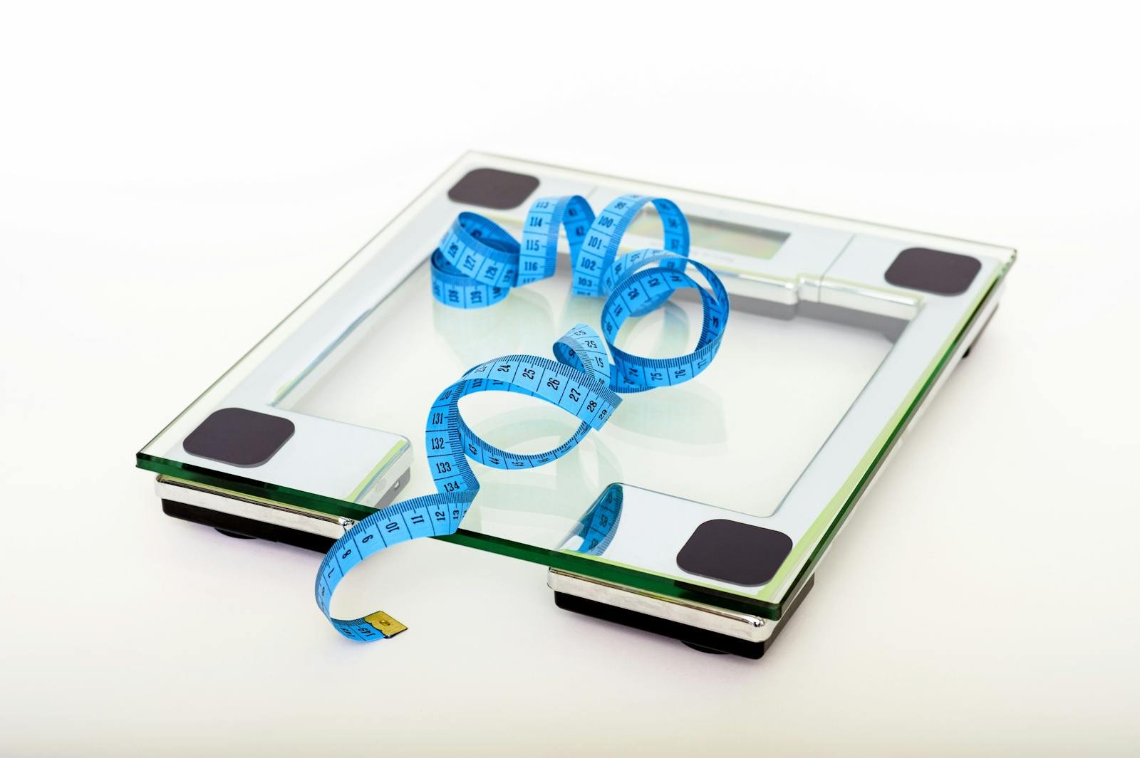 A digital glass weighing scale with a blue measuring tape, symbolizing weight management.