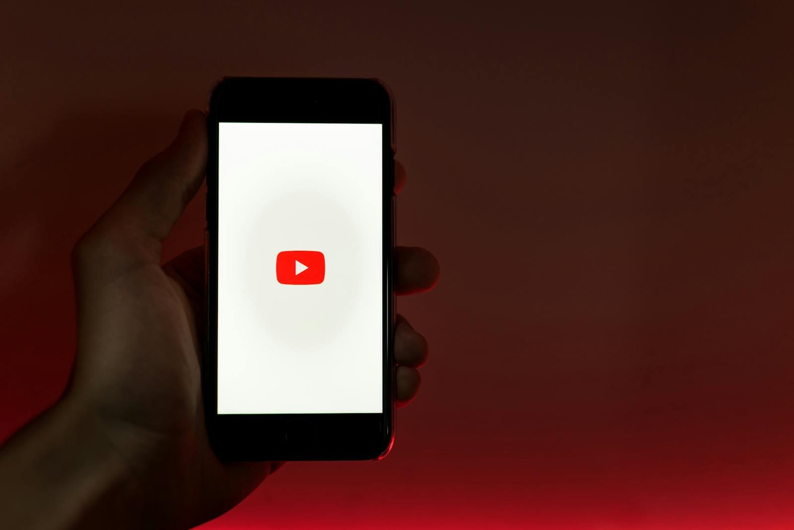 A hand holding a smartphone displaying the YouTube app against a red background.