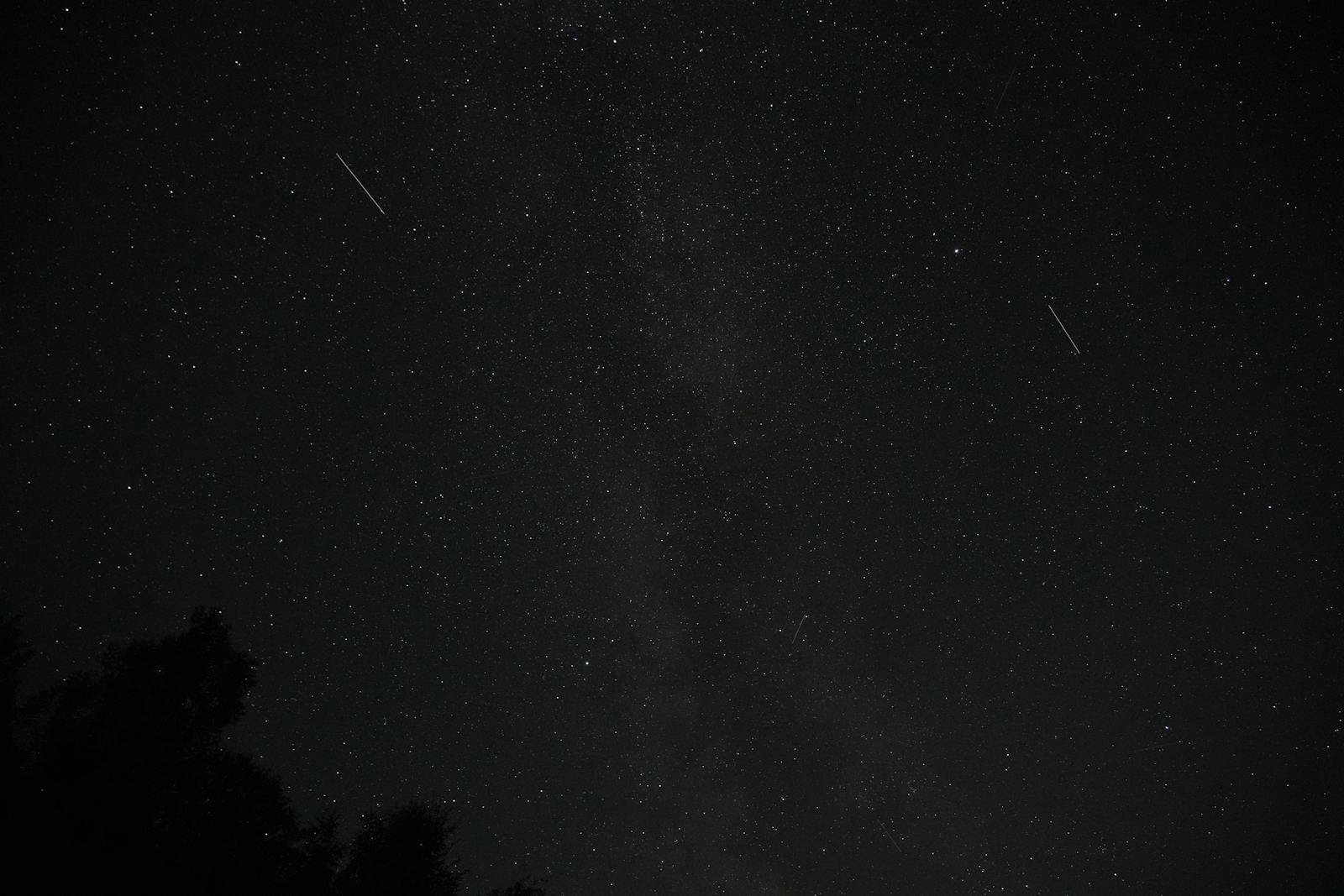 A dark night sky filled with stars and visible shooting stars.