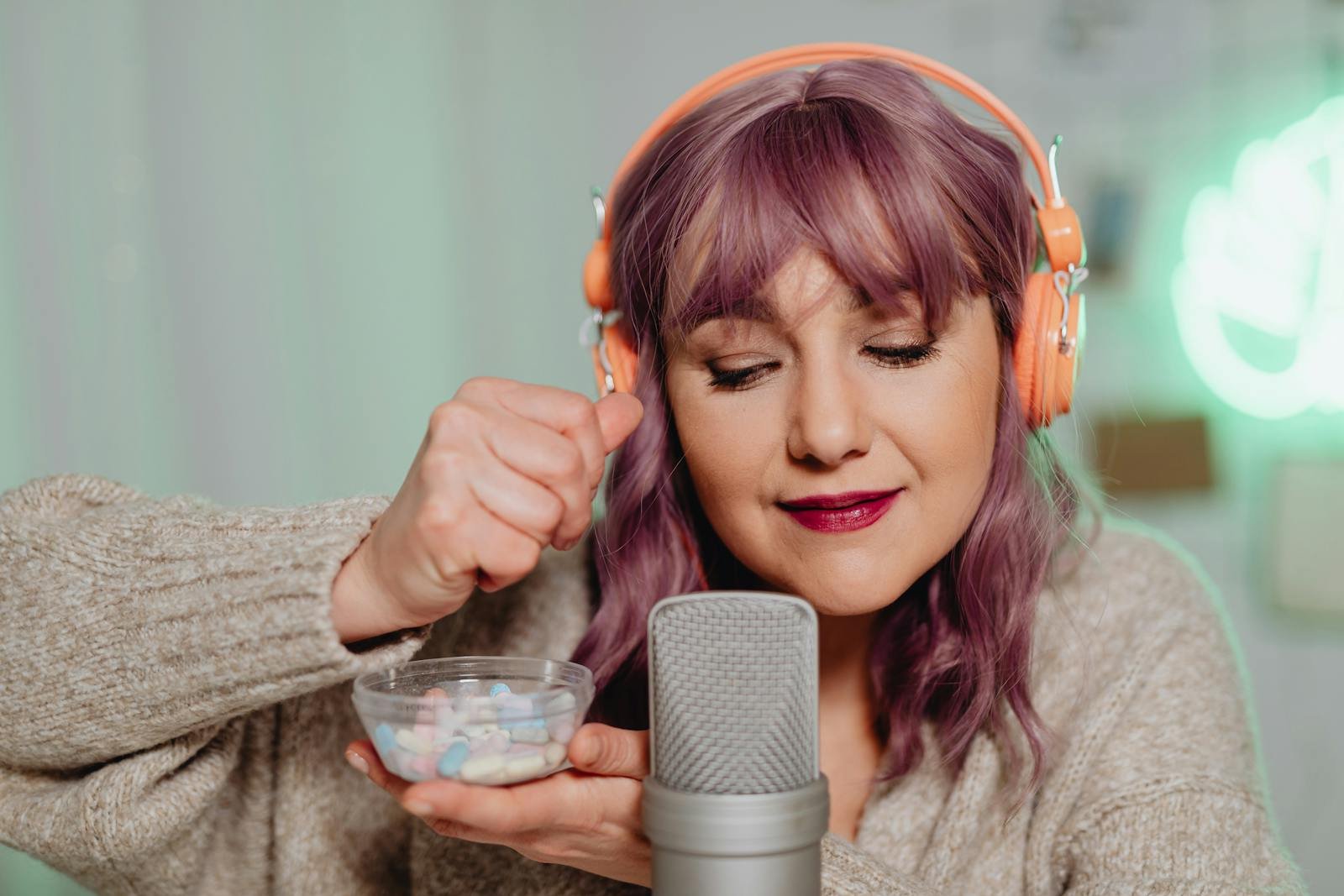 A woman with purple hair and headphones recording ASMR using a microphone indoors.
