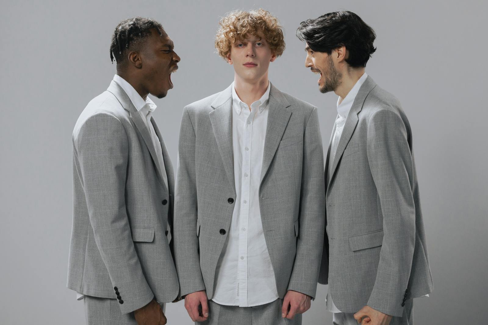 Three men in gray suits demonstrating conflict in a professional setting.